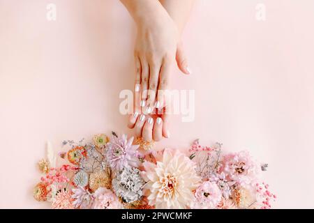 Vista dall'alto del raccolto femminile irriconoscibile con fiori in fiore che dimostrano una manicure elegante e ordinata su sfondo rosa Foto Stock