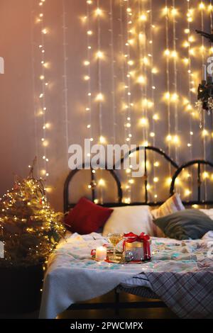Vassoio con decorazioni e scatola regalo posta su comodo letto in camera da letto accogliente decorato per Natale celebrazione di notte Foto Stock
