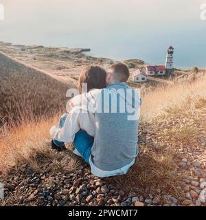 Una coppia romantica vestita di comodi pullover insieme vicino al faro al tramonto Foto Stock