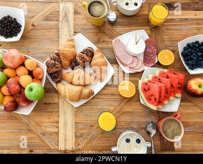 Angolo elevato di sana colazione su tavola di legno al mattino, assortimento di vari deliziosi piatti di farinata d'avena con latte, croissant appena sfornati, frutta Foto Stock