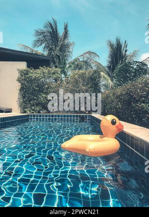 Anatra giallo anello gonfiabile galleggiante in piscina circostante con palme in caldo giorno di sole estate sul cortile della casa moderna vacanza o. Foto Stock