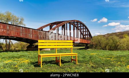 Panca di legno giallo sovradimensionato di fronte al vecchio ponte ferroviario, iscrizione Benvenuto, campagna contro la carenza di lavoratori qualificati, marketing locale Foto Stock