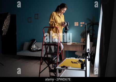 Fotografo femminile che ha configurato la fotocamera in studio domestico. Blogger moderno. Creatore di contenuti. Donna che scatta foto. Foto Stock