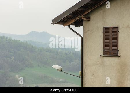 Vista panoramica sulle colline da un'antica casa con tetto in legno, finestra e lampione nel Castello di San Sebastiano da po, Torino, Piemonte, Italia Foto Stock