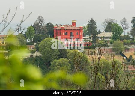 Vista panoramica sulle colline con vegetazione verde e un castello rosso o edificio dal Castello di San Sebastiano da po, Torino, Piemonte, Italia Foto Stock