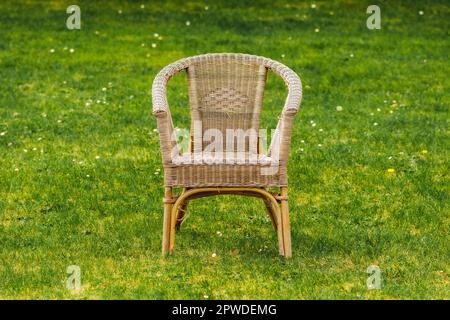 Vecchia sedia vuota in vimini su prato verde e fiori primaverili Foto Stock