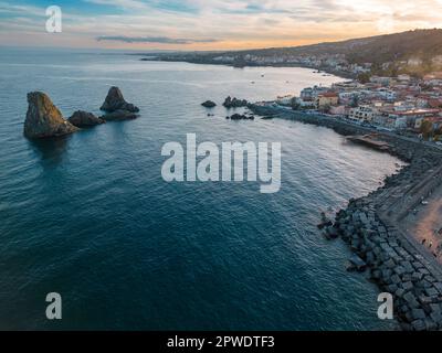 Splendida vista aerea delle pile di Acitrezza sulla costa siciliana, catturata da un drone durante un vivace tramonto. Foto Stock