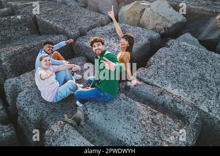 Un gruppo di quattro amici diversi festeggia insieme, facendo gesti di mani gioiose mentre si guarda la fotocamera. Ripresa aerea del drone. Foto Stock