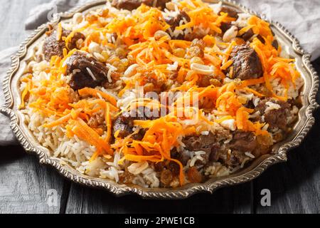 Piatto nazionale afghano Kabuli Pulao riso pilaf con agnello e uva passa, carota, noci, spezie primo piano sul piatto sul tavolo di legno. Orizzontale Foto Stock