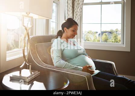 Non vedo l'ora di tenerti tra le braccia. una donna incinta seduta in salotto da sola. Foto Stock