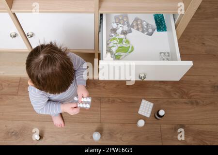 Il bambino del bambino ha aperto il cassetto dell'armadietto con le pillole e la medicina. Bambino che tiene una confezione di pillole nel salotto di casa. Bambino di età un anno nove mese Foto Stock