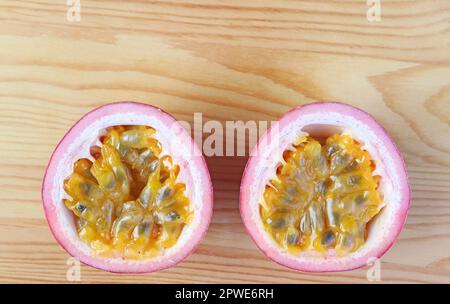 Vista dall'alto dei frutti della Passione freschi maturi tagliati a metà, isolati su sfondo di legno Foto Stock