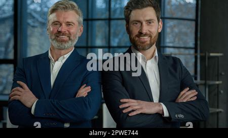 Due uomini d'affari sorridenti di successo in posa insieme a braccia incrociate uomo giovane e maturo partner commerciali colleghi dipendenti aziendali Foto Stock