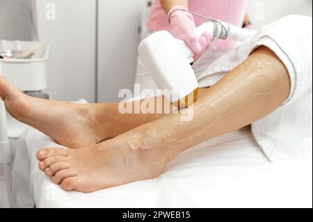 Cosmetologia estetica. Epilazione laser e cosmetologia. Procedura cosmetologica di rimozione dei capelli. Donna caucasica che fa una procedura per rimuovere i capelli indesiderati sulle gambe utilizzando un laser in un salone di bellezza Foto Stock