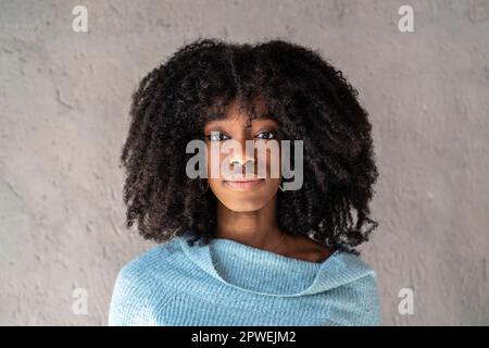Ritratto di felice ragazza afroamericana - capelli ricci donna cubana con piercing al naso che posa di fronte alla macchina fotografica su uno sfondo grigio - giovane Foto Stock