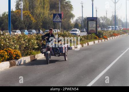 Strada del Tagikistan. 17 ottobre 2019: Giovane uomo cavalcare su una vecchia moto con un carrello laterale. Foto Stock