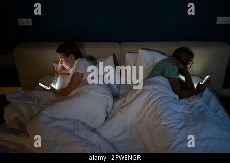 Famiglia coppia diversa a letto con smartphone marito e moglie si sono allontanati l'uno dall'altro. Foto Stock