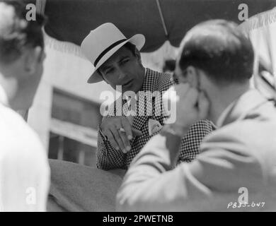 L'attore americano GARY COOPER chattò con un paio di uomini nei giardini degli studi della Paramount a Hollywood nel 1934. È vestito con il suo costume per ORA E PER SEMPRE in cui ha recitato con CAROLE LOMBARD e SHIRLEY TEMPLE. Pubblicità della Paramount Pictures. Foto Stock