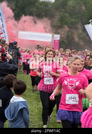 Race for Life Runners che partecipa per raccogliere fondi per beneficenza indossando t-shirt rosa che si allontanano dalla linea di partenza con gli spettatori che li incoraggiano Foto Stock