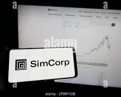 Persona che tiene il telefono cellulare con il logo della società danese di software finanziario SimCorp COME sullo schermo di fronte alla pagina web. Messa a fuoco sul display del telefono. Foto Stock