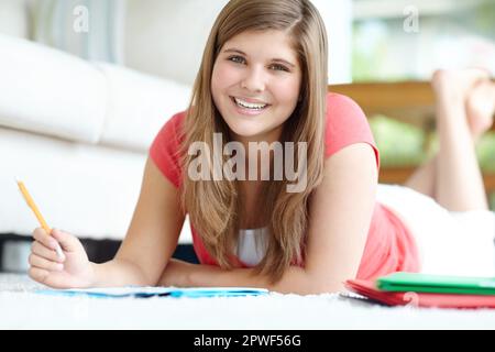 Shes uno studente. Un grazioso studente che fa i compiti mentre si trova sul pavimento della sua camera da letto. Foto Stock