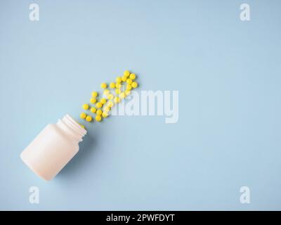 Minimalismo modello di stile per blog medico. Bottiglia bianca della medicina e piccole pillole rotonde gialle rovesciate fuori fondo di carta blu. Farmaceutico e. Foto Stock