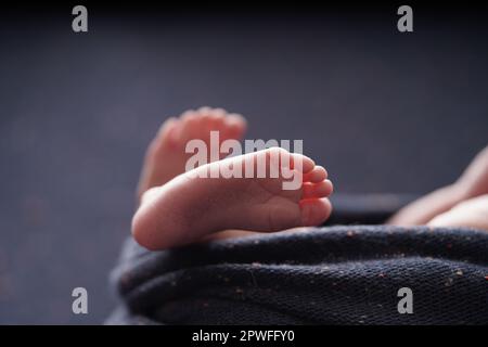 Piccolo bambino a piedi nudi attraversato su una coperta di sfondo blu marino. vista ravvicinata del piede del bambino il bambino è comodamente avvolto in una coperta blu. newb Foto Stock