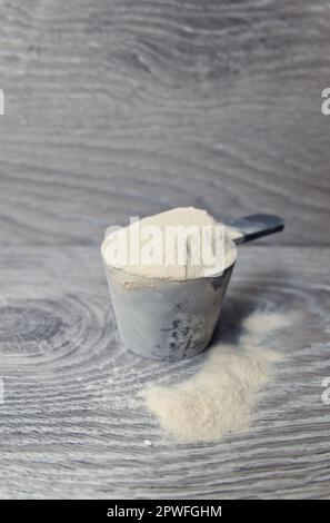 Primo piano di polvere di proteina del siero di latte nel misurino su fondo di legno grigio Foto Stock