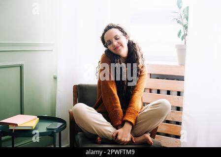 Giovane donna che si sente gioiosa e rilassata a casa. Donna felice godendo una giornata accogliente a casa. Donna sorridente che si sente soddisfatto e rilassato nel suo moderno Foto Stock