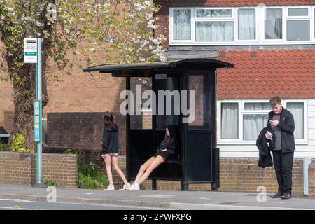 Persone che aspettano a una fermata dell'autobus, tra cui un giovane e due adolescenti, Surrey, Inghilterra, Regno Unito. Vita quotidiana, trasporti pubblici, 2023 Foto Stock