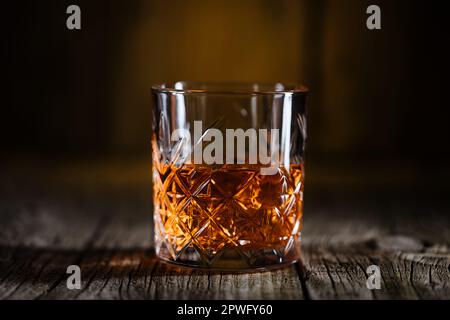 Whiskey con ghiaccio o brandy in un bicchiere su un tavolo rustico in legno. Frullare con ghiaccio in un bicchiere. Whiskey o cognac in un bicchiere. Messa a fuoco selettiva. Foto Stock