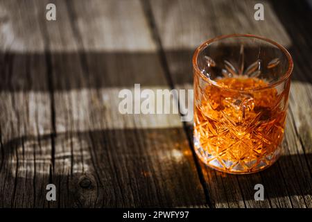 Whiskey con ghiaccio o brandy in un bicchiere su un tavolo rustico in legno. Frullare con ghiaccio in un bicchiere. Whiskey o cognac in un bicchiere. Messa a fuoco selettiva. Foto Stock