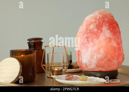 Lampada al sale Himalayana, candele e cristalli su tavolo dorato vicino a parete grigio chiaro Foto Stock