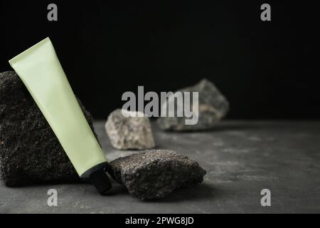 Tubo di crema per le mani tra le pietre su un tavolo grigio su sfondo scuro. Modello per il design Foto Stock