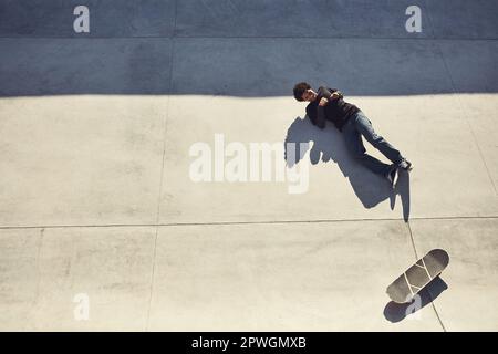 Cadere è parte del gioco. Colpo ad angolo alto di un giovane sdraiato sul pavimento accanto al suo skateboard in uno skatepark. Foto Stock