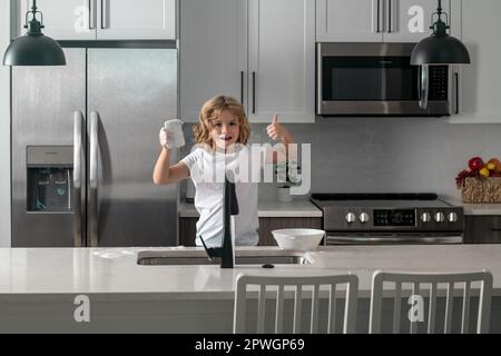 Divertenti ragazzi gemelli che aiutano in cucina con piatti di lavaggio. Bambini che si divertono con i lavori di casa. Bambino ragazzo lavare piatti in cucina interno. Bambino Foto Stock