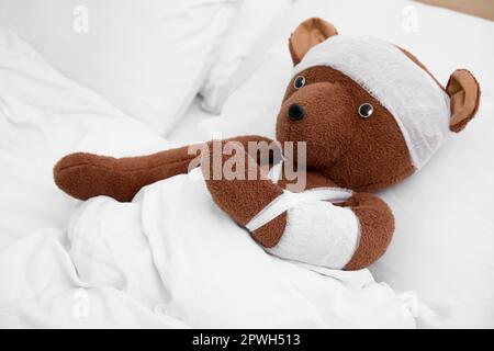 Orso giocattolo con bende sdraiate a letto Foto Stock