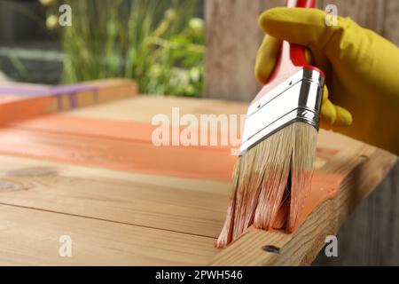 Lavoratore che applica vernice corallo su superficie di legno contro sfondo sfocato, primo piano. Spazio per il testo Foto Stock