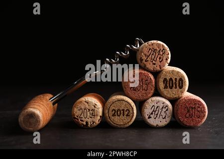 Cavatappi e tappi di vino con date diverse su tavola di ardesia, primo piano Foto Stock