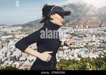 Andare comporta un passo alla volta. una giovane donna determinata che va per una corsa da sola con una vista della città sullo sfondo. Foto Stock