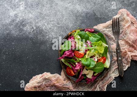 Insalata vegana verde di lattuga radicchio, fregio, rucola e spinaci su fondo nero. Cibo sano. Vista dall'alto Foto Stock