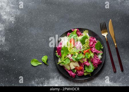 Insalata vegana verde di lattuga radicchio, fregio, rucola e spinaci su fondo nero. Cibo sano. Vista dall'alto Foto Stock