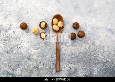 Noce macadamia naturale in un cucchiaio di legno. Noce sbucciato. Ingrediente sano per cosmetici e alimenti. Vista dall'alto su sfondo grigio. Foto Stock