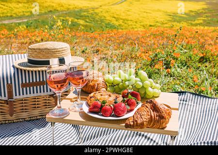 Romantico pic-nic primaverile sul prato fiorito, vino rosa fragola e croissant Foto Stock