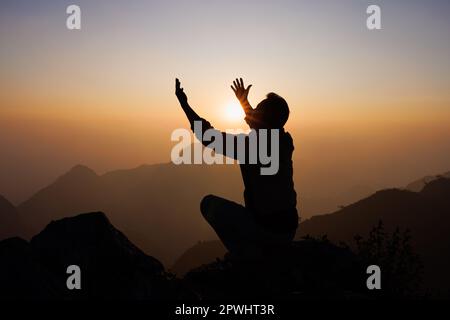 La silhouette di un uomo sta pregando Dio sulla montagna. Pregare le mani con fede nella religione e credere in Dio su sfondo di benedizione. Potere della speranza o. Foto Stock