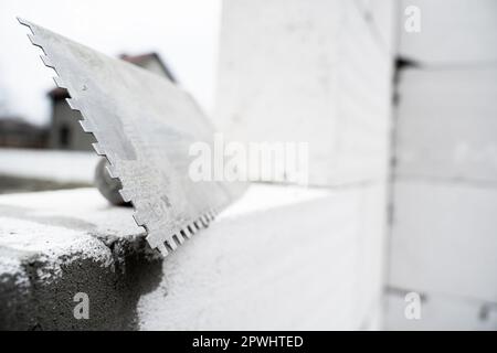 Cazzuola con intaglio sullo sfondo di un edificio in mattoni di cemento aerato primo piano, foto in bianco e nero Foto Stock