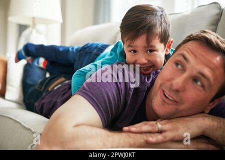 HES il papà più impressionante del mondo. un adorabile ragazzino e suo padre giocano insieme sul divano di casa. Foto Stock