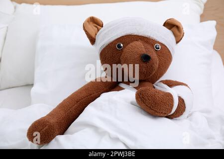 Orso giocattolo con bende sdraiate a letto Foto Stock