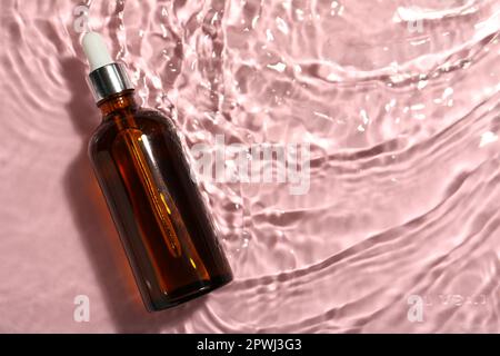 Bottiglia di olio idrofilo in acqua su sfondo rosa, vista dall'alto. Spazio per il testo Foto Stock