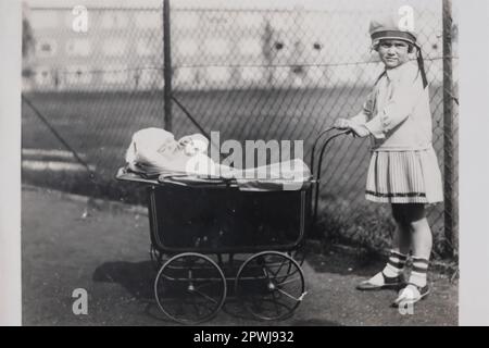 La bambina spinge il passeggino con il fratello del bambino nel 1927 Foto Stock